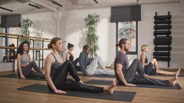 Group of mixed-race people with their coach intensively training in modern fitness studio. Actively practicing yoga together. Improving physical or mental well being. Concept of yoga.