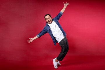 Full length portrait of a cheerful young man standing on toes dancing lean back having fun spreading hands isolated on red background