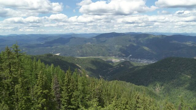 High wide aerial above Kellogg Idaho in summer from forest mountain peaks