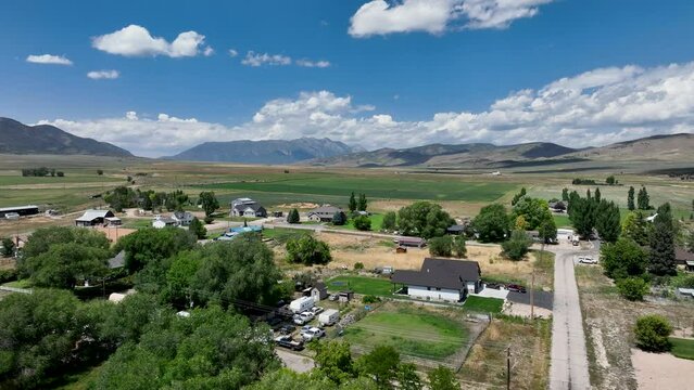 Aerial rural city homes mountain valley summer Utah 2. Farming community agricultural economy. Spring summer weather mountain valley green agriculture field. Homes, barns, buildings.