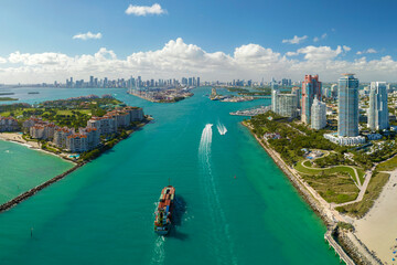 Aerial view of large container ship entering in Miami harbor main channel near South Beach. Luxurious hotels and apartment buildings on waterfront and high skyscrapers of downtown in distance - obrazy, fototapety, plakaty