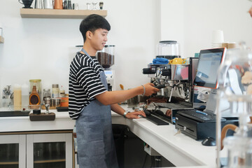 Young cheerful barista wearing apron while preparing coffee at an automatic machine in a modern coffee shop.