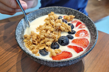 Bowl of homemade granola with yogurt and fresh berries on wooden table
