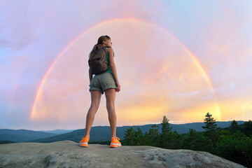 Young woman hiker standing alone on mountain footpath enjoying view of evening nature on wilderness trail. Active way of life concept