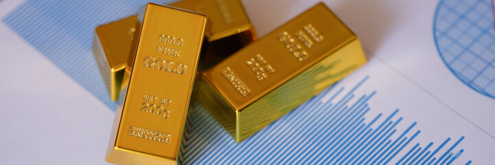 Gold bars on financial reports and charts close up.