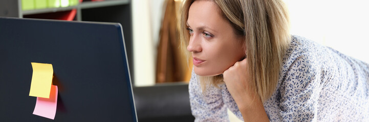 Business woman standing at her working desk and looks at computer monitor.