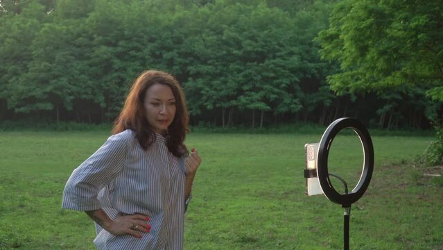 blogger is recording videoblog standing in forest meadow talking to subscribers. Social media and people concept.