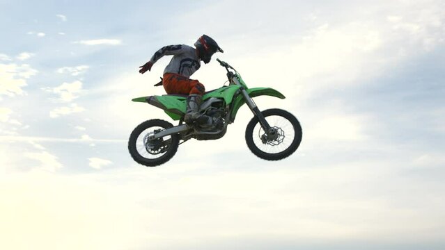 Dirtbiker jumping natural sand dunes and does no hander trick - Slow motion