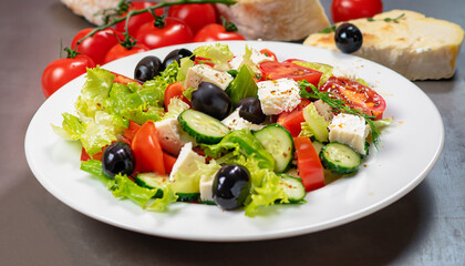 Mediterranean cuisine dish Greek salad of fresh raw cucumbers, tomatoes, bell peppers, black olives and lettuce leaves with fresh fetu cheese chunks