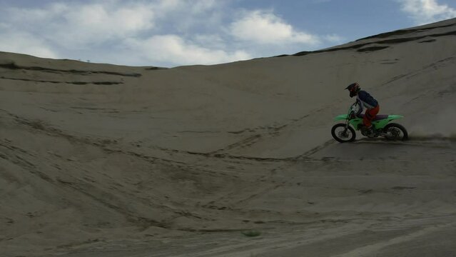 Motocross dirt biker wheelies and rides a berm at a sand quarry - summer day