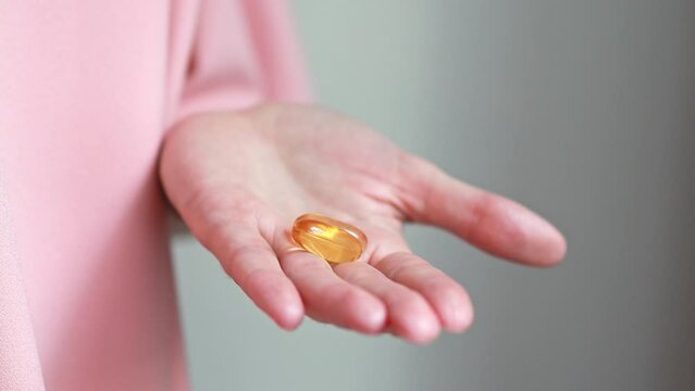 Close-up of two capsules of omega-3 nutritional supplement or fish oil or vitamin D3 in a woman's palm