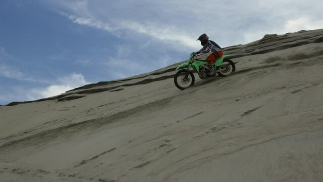 Motocross dirtbiker jumping into berm then speeding away kicking up sand - power sports