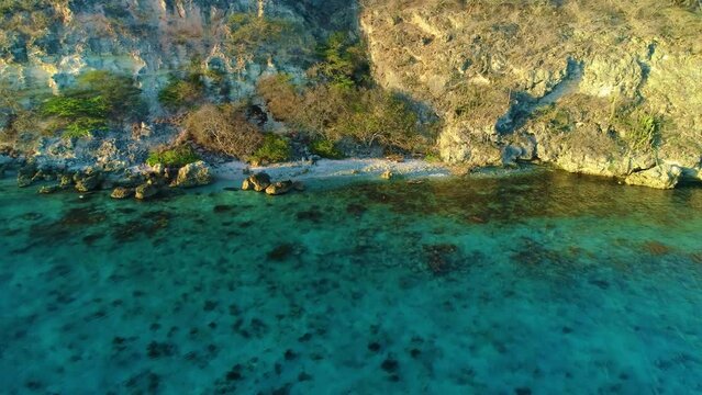 Stunning secluded caribbean beach at base of tall cliffs, white sand golden hour light