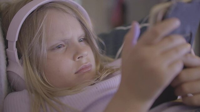 A young European girl wearing headphones and transfixed by her digital device