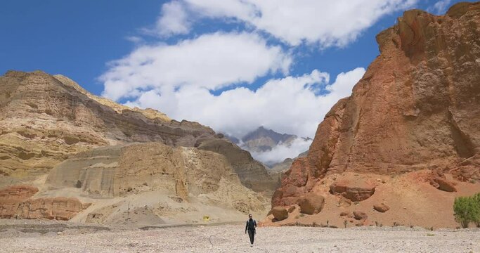 In Upper Mustang Nepal, A tourist walks infront of Huge muddy rock mountains under the Blue cloudy sky. Enjoying nature around tourist feels refreshed. peace and calm 4K