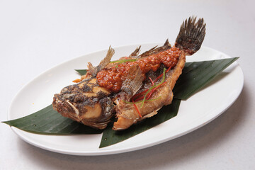 deep fried whole red grouper fish seafood with peranakan nonya spicy chilli sambal asam sauce in leaf plate on white background fusion asian halal menu for restaurant