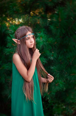 Portrait of a beautiful little elf girl with long hair in a long green dress.