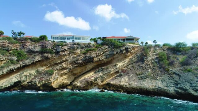 Drone rises towards angled eroded rock of caribbean island, stunning home on cliff edge