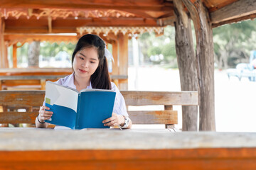 Asian girl student sitting at a wooden table reading a book. Students back to school. Asian cute girl in White uniform looking at the book.