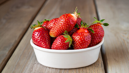 Fresh strawberries in a white porcelain bowl on wooden table in rustic style, selective focus