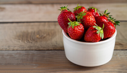 Fresh strawberries in a white porcelain bowl on wooden table in rustic style, selective focus