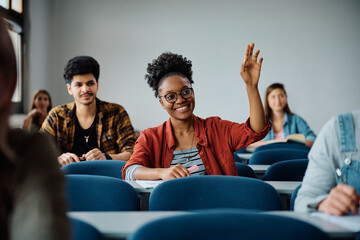 Happy black student raising her hand to ask question during class at university.