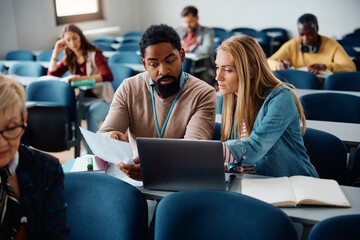 Black adult education teacher assists his student with an assignment during class in classroom.