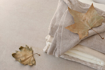 Wool knitted sweaters stack in neutral nude colors, light brown fall leaves on beige table....