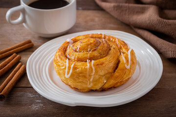 Cinnamon roll bun on white plate and cup of coffee