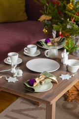 Coffee serving with white tableware for Christmas on a table near a dark pink sofa. Christmas concept, table setting