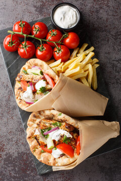 Tasty wrapped greek chicken gyros with vegetables, french fries and tzatziki sauce closeup on the board on the table. Vertical top view from above