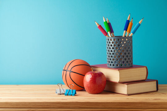 Back to school concept with pencils, basketball ball and books on wooden table over blue background