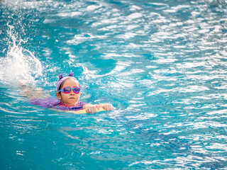 Asian child or kid girl wearing swimming suit to learning on swimming pool , learn and training swim on kick board