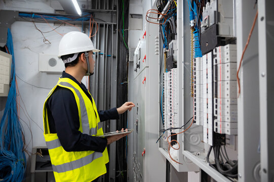 Electrical Engineer team working front control panel, An electrical engineer is installing and using a tablet to monitor the operation of an electrical control panel in a factory service room..