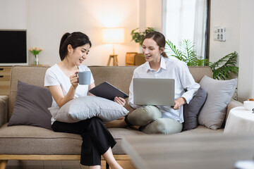 Two roommates woman sitting on a sofa in the living room at home, Friendship and sisterhood concept.