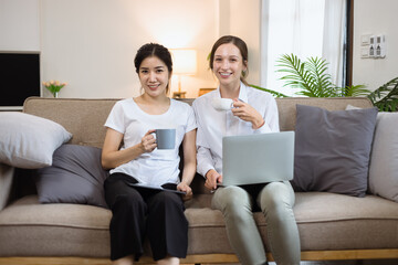 Two roommates woman sitting on a sofa in the living room at home, Friendship and sisterhood concept.