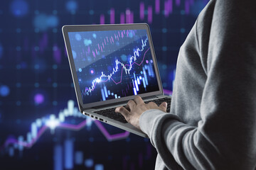 Close up of hacker hands using laptop with glowing growing forex chart on blurry background. Trade, hacking, finance and stock market concept.