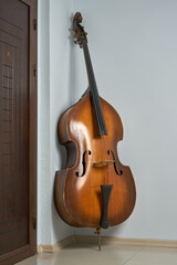 An old double bass leaning on a white wall.