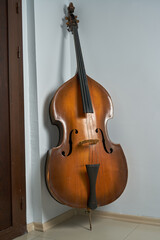 An old double bass leaning on a white wall.