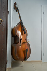 An old double bass leaning on a white wall.