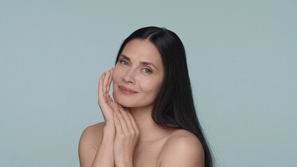 Obraz premium Portrait of a contented seminude woman on a blue background closeup. Woman with natural makeup, clean and smooth skin. Beauty concept. Natural beauty, cosmetology, skin care.