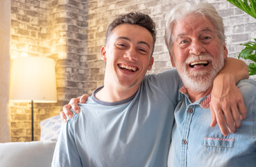 Portrait of family couple, a young boy and his old grandfather smiling looking at camera while sitting on the sofa at home, old and new generation - caring for the people we love