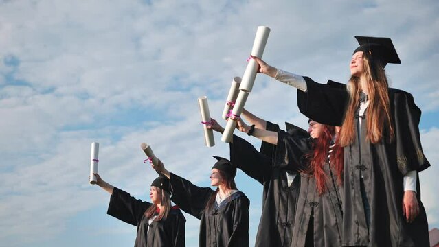Cheerful graduates pose with raised diplomas on a sunny day.