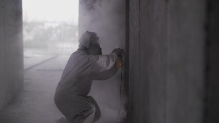 A construction worker in a protective suit polishes concrete walls