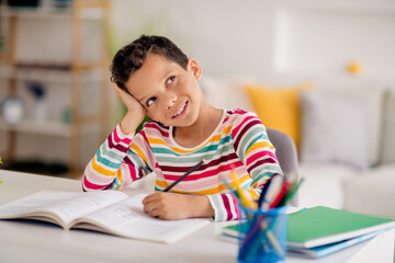 Photo of dreaming cute son school boy touch head looking interested thoughtful write essay test...
