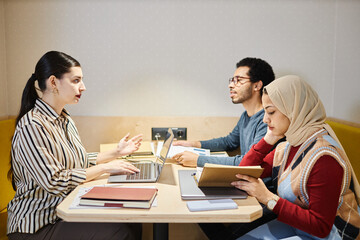 Obraz premium Side view at group of Middle Eastern business people meeting at table in booth with electric lighting, copy space