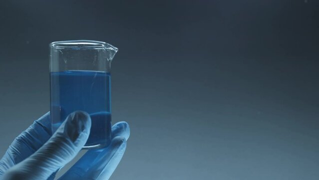 Lab assistants hold a flask. Blue liquid solution at clinic. Glass flask in blue research chemistry science banner dark background. Chemical experiment concept. Laboratory equipment.