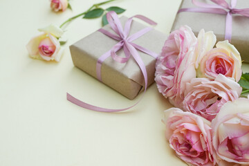 Concept background with light pink roses and wrapped kraft gift box on beige background. Flower card. Holiday, congratulations, happy mothers day. International Women's day. Side view.