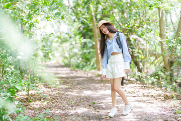 Cute Asian woman with long hair wearing hat walking in community forest, park which is a rural nature education center. relax and relieve the exhaustion from working all week during the long weekend.