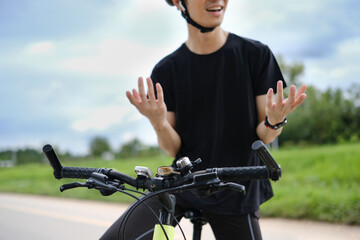 Asian male cyclist wearing wireless earphones talking on mobile phone while cycling in the park